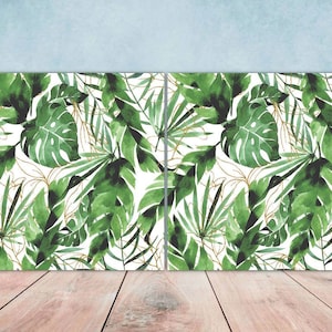 Peut inclure: Deux aquarelles de feuilles tropicales sur fond blanc. Les feuilles sont vertes et ont un contour doré. Les peintures sont encadrées et accrochées à un mur.