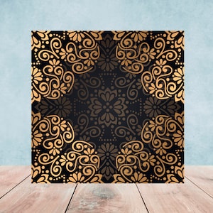 May include: A square black and gold patterned background with a repeating design of stylized flowers and swirls. The background is on a wooden surface.