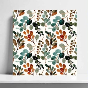 以下が含まれることがあります： 植物の枝を描いた水彩画風の繰り返し模様が特徴の正方形のウォールアート。白地の上に、ティール、セージグリーン、ダークフォレストグリーン、バーントオレンジの色合いで、楕円形の葉と小さな丸い実が描かれています。