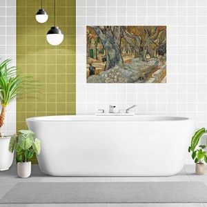May include: A white bathtub with chrome fittings sits in a bathroom with white and green tiled walls. A painting of a landscape with trees hangs above the tub. Two potted plants are on the floor next to the tub.