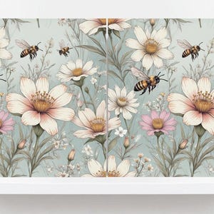 May include: A floral pattern featuring large white and pink flowers with yellow centres, interspersed with smaller white flowers and green foliage. Honeybees are depicted in flight. The background is a soft, muted blue-green.