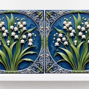 以下が含まれることがあります： 白い花柄の青いセラミックタイル2枚。タイルには、白い花と緑の葉を持つ、様式化されたスズランの花が描かれています。