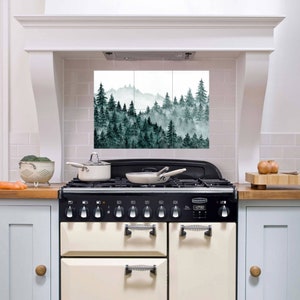 May include: A white kitchen with a black and cream range stove. The backsplash is decorated with a watercolor print of a misty forest scene.