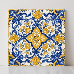 May include: Square canvas art with a symmetrical floral design in blue and yellow. The artwork displays a central yellow flower surrounded by blue and yellow floral patterns against a cream background. The design is reminiscent of traditional tile work.