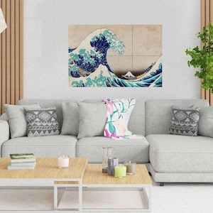 May include: A grey sectional sofa with two throw pillows and a floral throw blanket. A large print of The Great Wave off Kanagawa hangs on the wall above the sofa. The sofa is in a living room with a wooden floor and a coffee table in front of it.