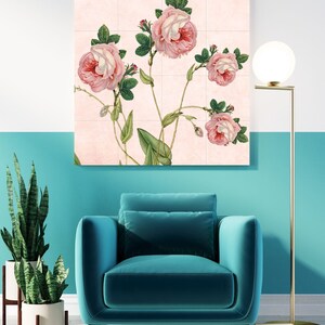 May include: A pink floral print with five pink roses on a light pink background. The print is framed and hanging on a wall above a teal blue armchair.