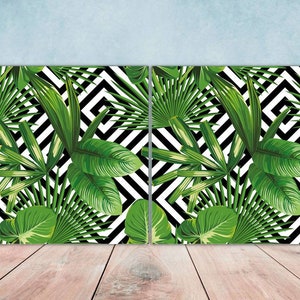 Op de afbeelding: Twee rechthoekige wandkunstwerken met een tropisch bladerenontwerp. De bladeren zijn in verschillende groentinten, tegen een zwart-wit geometrisch zigzagpatroon. Het kunstwerk wordt gepresenteerd op een licht houten oppervlak.