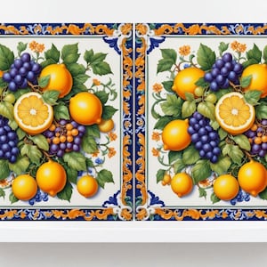 May include: Two square ceramic tiles with a blue and gold border. The tiles feature a white background with a cluster of lemons, grapes, and green leaves.