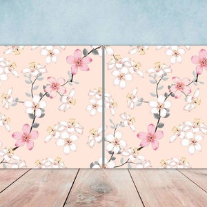 May include: Two square canvases with a pink and white floral pattern. The floral pattern features pink flowers with white centers and white flowers with yellow centers. The background is a light peach color.