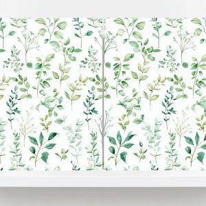 May include: A white shelf displays botanical wallpaper featuring a repeating pattern of green leaves and stems. The leaves vary in shades of green, creating a natural aesthetic. The wallpaper is mounted on a white wall.