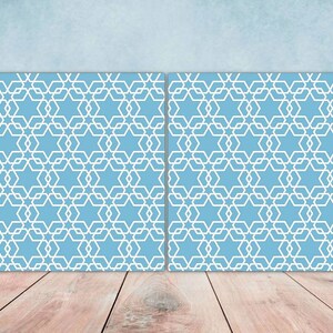 May include: Two blue square panels with a white geometric pattern of stars and interlocking circles. The panels are on a wood floor.