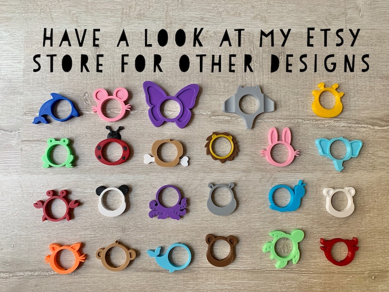 May include: A collection of 20 colorful silicone teethers in various animal and object shapes, including a butterfly, a crab, a turtle, a whale, a lion, a frog, a ladybug, a bunny, an elephant, an octopus, a monkey, a bear, and a dolphin.  The teethers are arranged in rows on a wooden surface.  "HAVE A LOOK AT MY ETSY STORE FOR OTHER DESIGNS" is written in black text at the top of the image.
