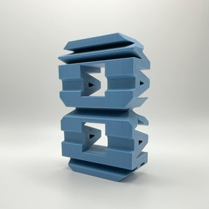 Pode incluir: Um objeto azul impresso em 3D com um design geométrico. O objeto é composto por duas peças empilhadas, cada uma com um furo quadrado no centro.
