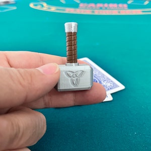 Op de afbeelding: Een zilverkleurige miniatuurhamer met een bruine houten handgreep. De hamer heeft een reli&euml;fdesign van een triquetra, een Keltisch symbool, op de kop.