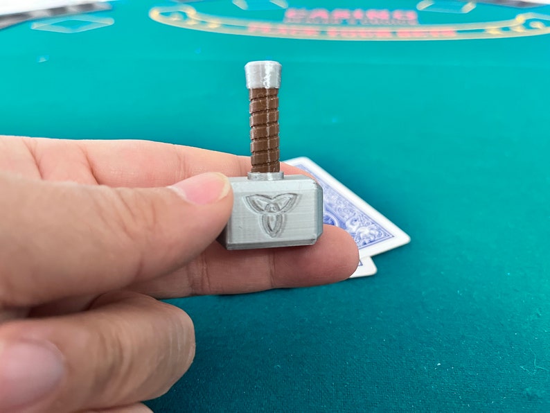 Op de afbeelding: Een zilverkleurige miniatuurhamer met een bruine houten handgreep. De hamer heeft een reli&euml;fdesign van een triquetra, een Keltisch symbool, op de kop.