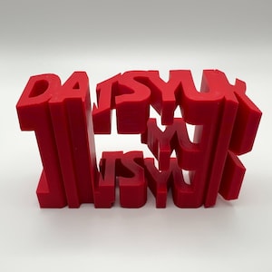 Könnte beinhalten: Eine rot 3D-gedruckte Skulptur des Wortes "DAISYUK" mit übereinander gestapelten Buchstaben.