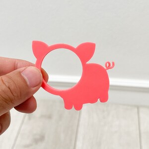May include: Pink plastic pig napkin ring. The pig has a round hole in the middle for a napkin.