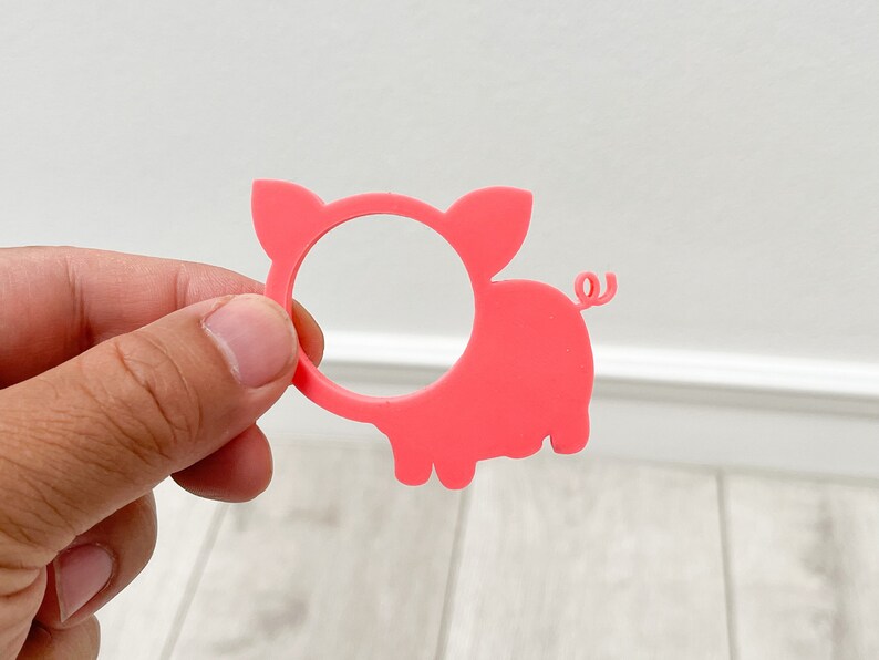 May include: Pink plastic pig napkin ring. The pig has a round hole in the middle for a napkin.
