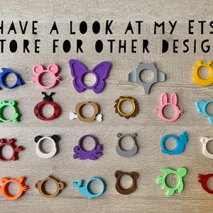 May include: A collection of 20 colorful silicone teethers in various animal and object shapes, including a butterfly, a crab, a turtle, a whale, a lion, a frog, a ladybug, a bunny, an elephant, an octopus, a monkey, a bear, and a dolphin.  The teethers are arranged in rows on a wooden surface.  "HAVE A LOOK AT MY ETSY STORE FOR OTHER DESIGNS" is written in black text at the top of the image.
