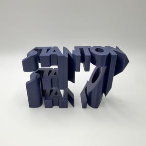 May include: A dark blue 3D printed object featuring the word STANTON in a bold, blocky, sans-serif font. The letters are connected in a stacked, multi-layered arrangement, creating a structural, geometric display piece with sharp, clean edges.