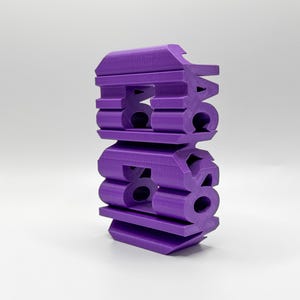 May include: A purple 3D printed object shaped like the word "BACK" stacked on top of the word "808".
