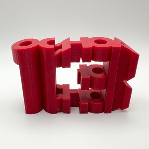 May include: A 3D printed red plastic sculpture of the word "SCHOOL" with the letters stacked on top of each other.