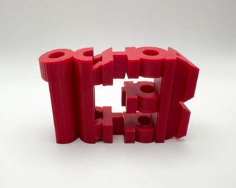 May include: A 3D printed red plastic sculpture of the word "SCHOOL" with the letters stacked on top of each other.