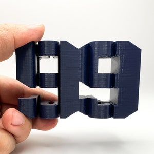 以下が含まれることがあります： 濃い青色の3Dプリントされた数字「99」。数字は複数の層で構成されており、表面にテクスチャがあります。