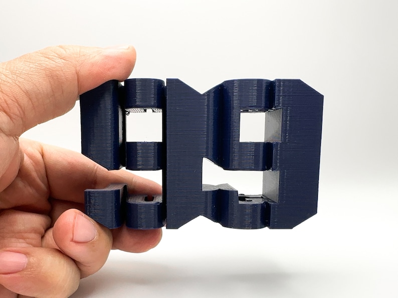 以下が含まれることがあります： 濃い青色の3Dプリントされた数字「99」。数字は複数の層で構成されており、表面にテクスチャがあります。