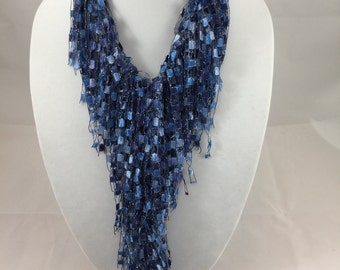 May include: A blue scarf with a textured, fringed design. The scarf is displayed on a white mannequin. The scarf's color transitions from lighter to darker shades of blue, creating a visually appealing accessory.