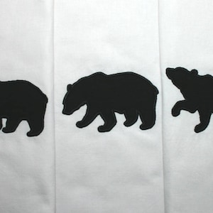 May include: Three black bear silhouettes are embroidered on a white fabric background. The bears are facing different directions and are all the same size.