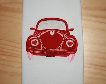 May include: Red embroidered car with pink accents and white hearts on the headlights. The car is a classic Volkswagen Beetle.