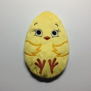 Könnte beinhalten: Ein gelber Plüsch-Küken in Form eines Eies mit gestickten Augen, Schnabel, Flügeln und Füßen.