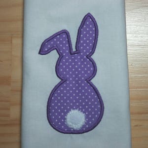 May include: Purple bunny applique with white polka dots and a white fluffy tail. The bunny is embroidered on a light blue fabric.
