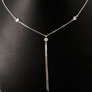 May include: A silver chain necklace with three small round clear stones. The necklace has a long, dangling chain with a stone at the end.