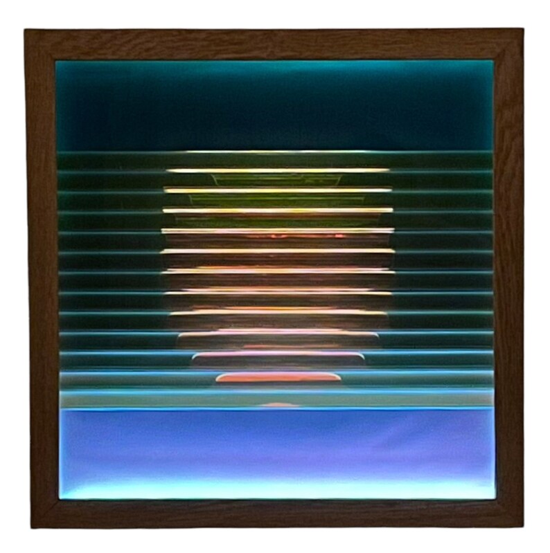 May include: A framed abstract artwork featuring a layered design of blue, green and orange glass panels. The artwork is set against a dark blue background.