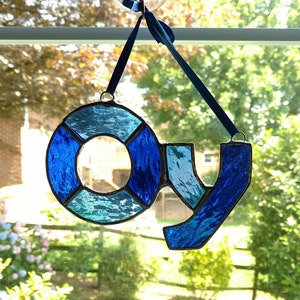 Op de afbeelding: Een hangend glas-in-loodraam met een blauw en wit ontwerp dat het woord "OY" spelt.