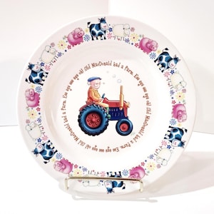 May include: White ceramic plate with a farm theme. The plate features a farmer driving a red and blue tractor, surrounded by cows, pigs, and sheep. The words "Old MacDonald had a farm" are written around the center.