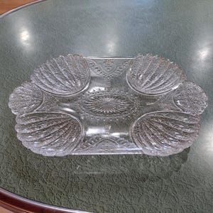 May include: A clear glass serving dish with a scalloped edge and a decorative pattern. The dish has four sections, each with a raised design.