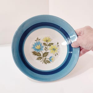 May include: A blue and white ceramic bowl with a floral design. The bowl has a blue rim and a white center with a yellow and blue flower design.