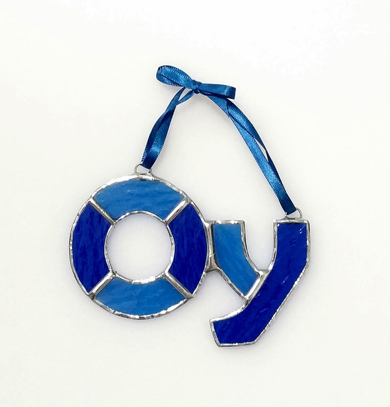 Op de afbeelding: Een ornament van gekleurd glas in de vorm van het woord "JOY" in blauwe en lichtblauwe tinten. De "O" is gevormd als een reddingsboei.