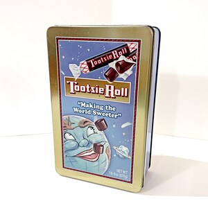 May include: A rectangular Tootsie Roll tin with a gold border. The front features the Tootsie Roll logo and the phrase "Making the World Sweeter." The tin has a blue background with illustrations of the Earth and Tootsie Rolls. Net weight is 1 lb 8 oz (679g).
