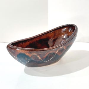 May include: A ceramic, oblong bowl with a glossy finish. The bowl features a blend of brown, dark blue, and white colors. The interior and exterior are smooth and reflective, suggesting a handcrafted pottery piece.