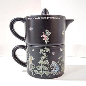 May include: Black ceramic teapot and teacup set. The teapot has a lid and a spout, with the text "A spot of tea to warm your thoughts." The set is decorated with floral and butterfly designs, and illustrations of Winnie the Pooh characters.