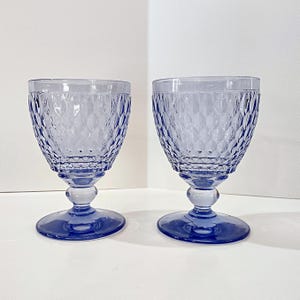 May include: Two blue-tinted wine glasses. Each glass features a diamond-patterned bowl, a small ball-shaped stem, and a circular base. The glasses are made of glass and are set against a white background.