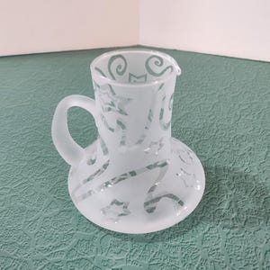 May include: A frosted glass pitcher with a handle and a swirling design etched into the surface.