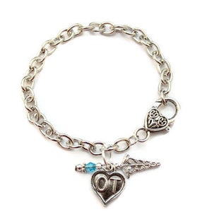 May include: Silver chain bracelet with a heart charm that says "OT" and a small blue crystal bead. The bracelet has a heart-shaped clasp.