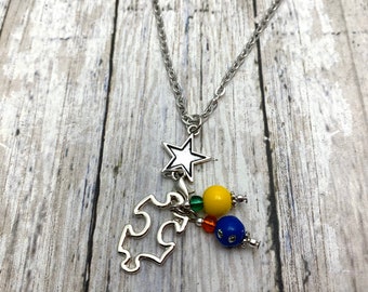 May include: A silver chain necklace with a silver puzzle piece charm, a silver star charm, and colorful beads. The beads are yellow, green, orange, and blue.