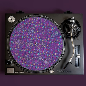 Könnte beinhalten: Eine lilafarbene Plattenteller-Unterlage mit einem Retro-Muster aus den 80er Jahren mit bunten Videospiel-Controllern, geometrischen Formen und pixelartigen Bäumen.