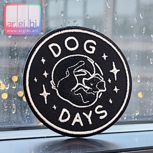 May include: Black and white embroidered patch with the text "DOG DAYS" in a circle. The center of the circle features a stylized image of a dog sleeping with stars around it.